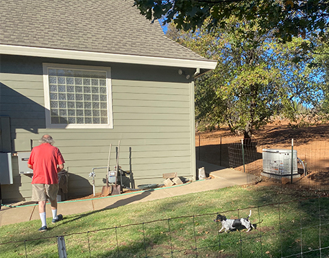 an elderly man enjoying his yard with his dog. in the distance is a generac generator